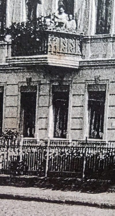 Zbliżenie na lewą część pocztówki z balkonem i budynkiem obok